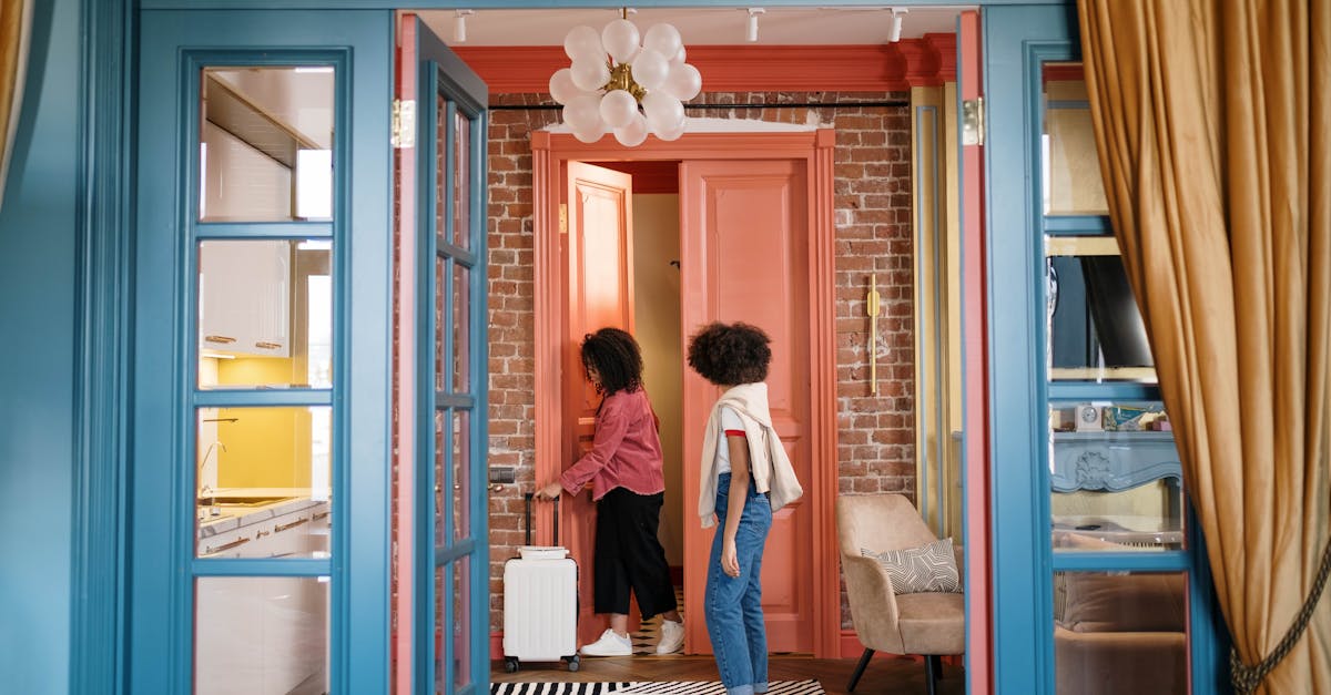 Stylish room with two women walking through doorway, carrying suitcase. Cozy and colorful decor.